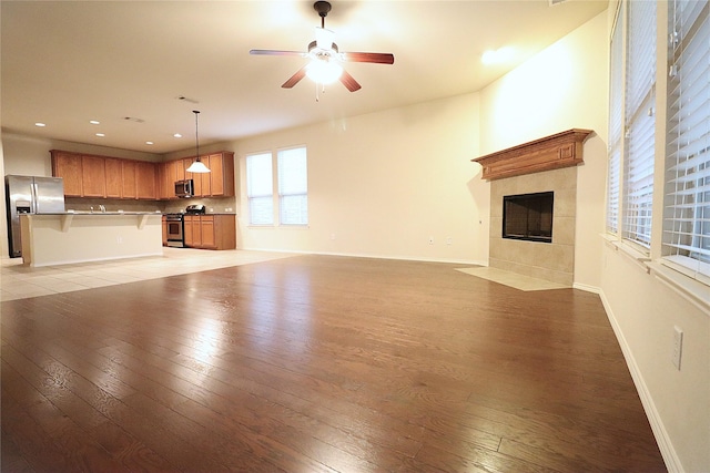 unfurnished living room featuring light wood-style floors, baseboards, ceiling fan, and a tiled fireplace