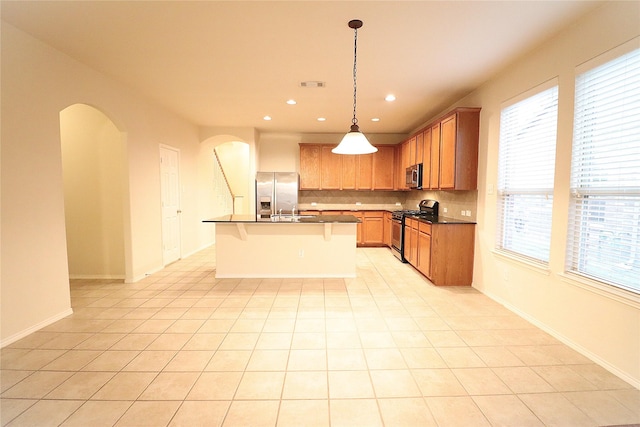 kitchen featuring decorative backsplash, dark countertops, a kitchen breakfast bar, arched walkways, and stainless steel appliances