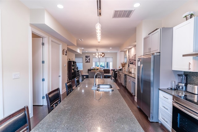 kitchen with visible vents, a sink, dark stone countertops, open floor plan, and stainless steel appliances