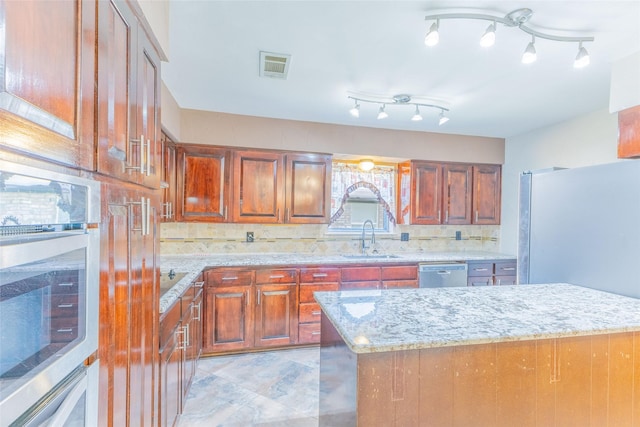 2418 Ingleside Dr, Grand Prairie, TX 75050 - kitchen featuring appliances with stainless steel finishes, a sink, decorative backsplash, light stone countertops, and brown cabinets