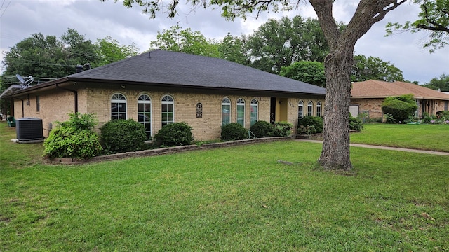 ranch-style house with central air condition unit, brick siding, a front yard, and roof with shingles