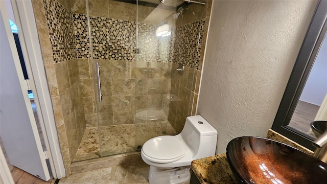 full bathroom with vanity, a textured wall, a tile shower, and toilet
