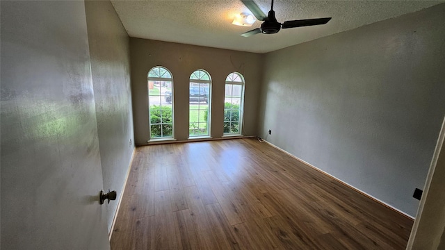 unfurnished room with a ceiling fan, a textured ceiling, wood finished floors, baseboards, and a textured wall