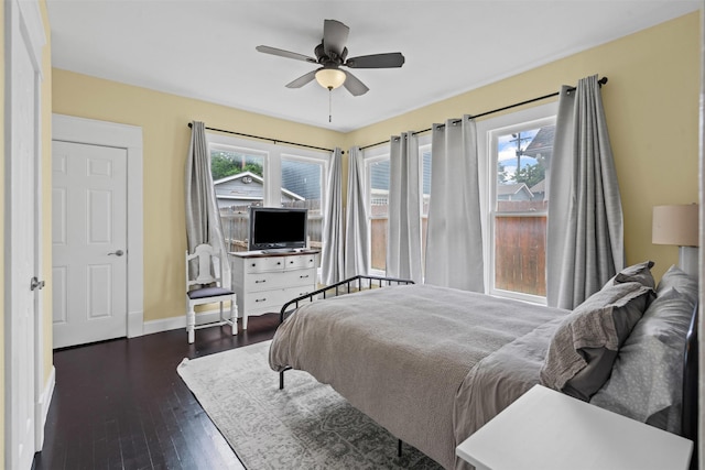bedroom featuring a ceiling fan, baseboards, dark wood finished floors, and multiple windows