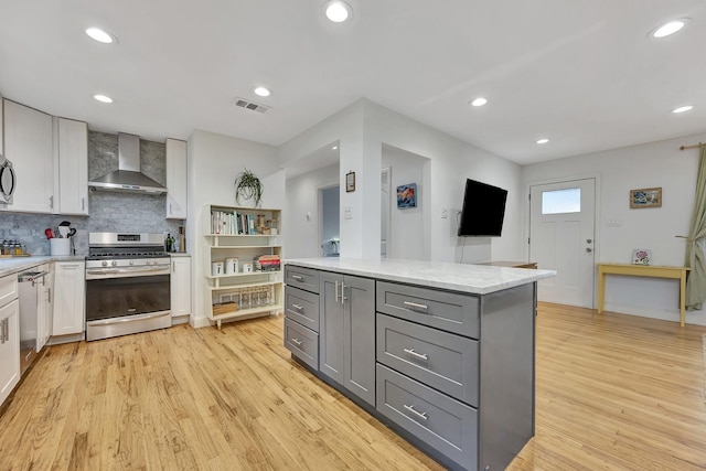 kitchen with stainless steel appliances, wall chimney range hood, gray cabinets, white cabinets, and light wood finished floors