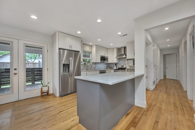 kitchen featuring appliances with stainless steel finishes, wall chimney range hood, a sink, a peninsula, and light wood-style floors