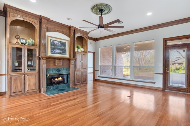 unfurnished living room featuring ceiling fan, a fireplace, baseboards, ornamental molding, and light wood-style flooring