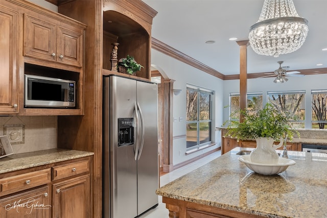 kitchen with appliances with stainless steel finishes, brown cabinetry, ceiling fan with notable chandelier, and tasteful backsplash