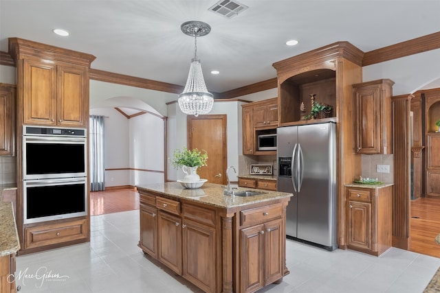 kitchen featuring visible vents, arched walkways, brown cabinets, a sink, and appliances with stainless steel finishes