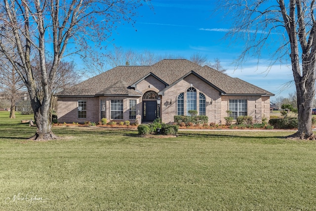 view of front of property featuring brick siding, roof with shingles, and a front yard