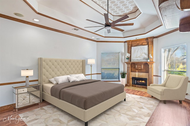 bedroom with a raised ceiling, a warm lit fireplace, wood finished floors, and visible vents