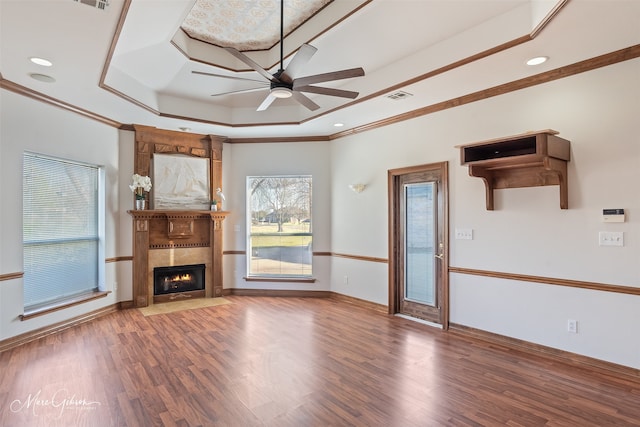 unfurnished living room featuring ceiling fan, visible vents, a fireplace with flush hearth, wood finished floors, and a tray ceiling
