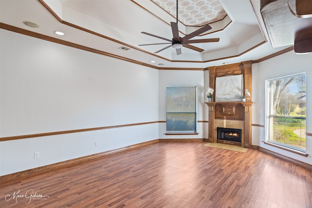 unfurnished living room featuring a ceiling fan, a fireplace, wood finished floors, ornamental molding, and a tray ceiling