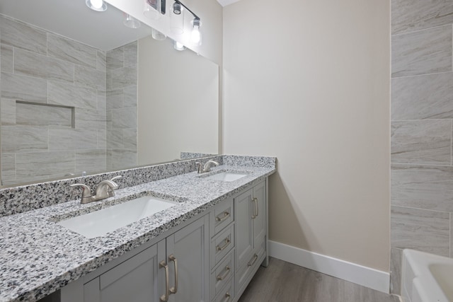 bathroom with double vanity, baseboards, a sink, and wood finished floors