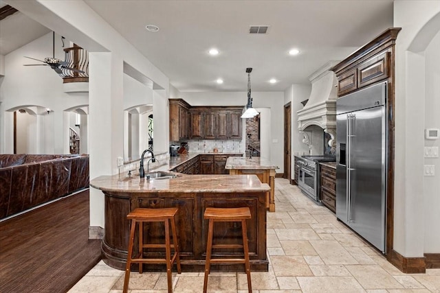 kitchen with visible vents, arched walkways, a sink, premium appliances, and custom range hood