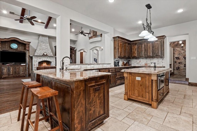 kitchen with ceiling fan, a kitchen island with sink, light stone countertops, a sink, and open floor plan