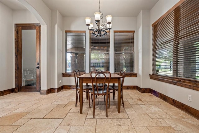 dining room featuring baseboards, stone tile floors, arched walkways, and a notable chandelier