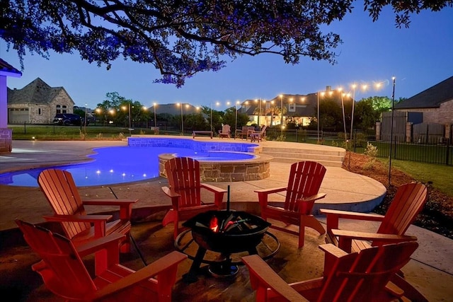 pool at night with fence, a fenced in pool, an outdoor hot tub, a patio, and a fire pit