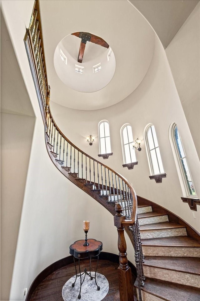 stairway with baseboards, wood finished floors, and a towering ceiling