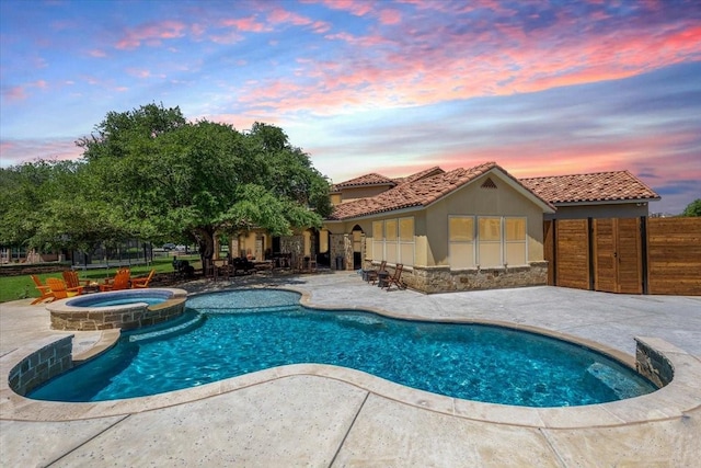 pool at dusk featuring a pool with connected hot tub, fence, and a patio area