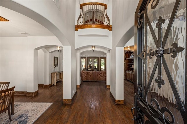 foyer entrance featuring visible vents, wood finished floors, baseboards, a high ceiling, and arched walkways