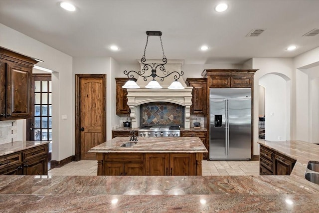 kitchen with visible vents, a kitchen island, light stone countertops, a sink, and stainless steel built in refrigerator