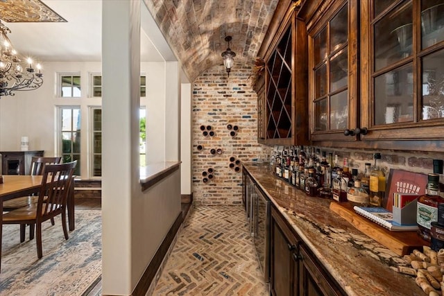 bar with a notable chandelier, brick floor, decorative light fixtures, baseboards, and lofted ceiling