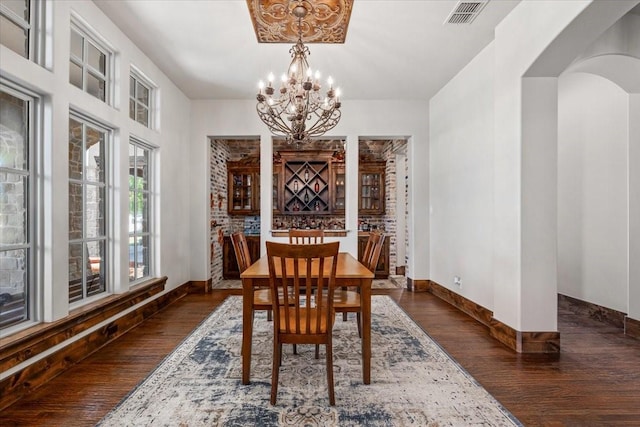 dining space featuring dark wood-style flooring, a notable chandelier, arched walkways, baseboards, and visible vents