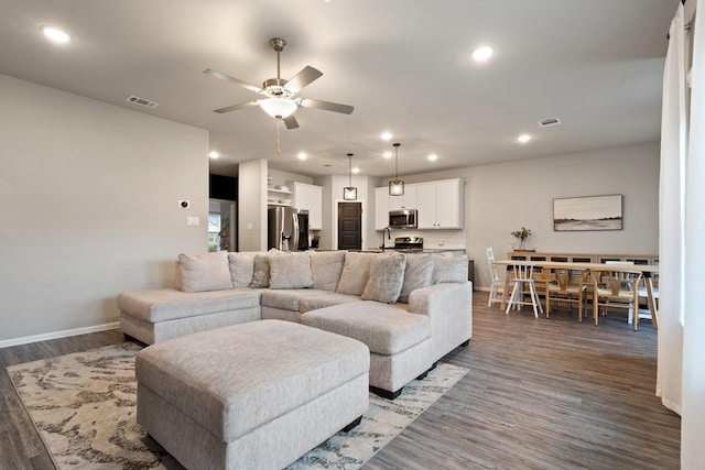 living room featuring a ceiling fan, visible vents, wood finished floors, baseboards, and recessed lighting