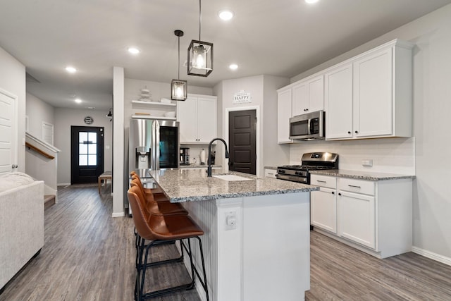 kitchen featuring wood finished floors, baseboards, white cabinets, a sink, and stainless steel appliances
