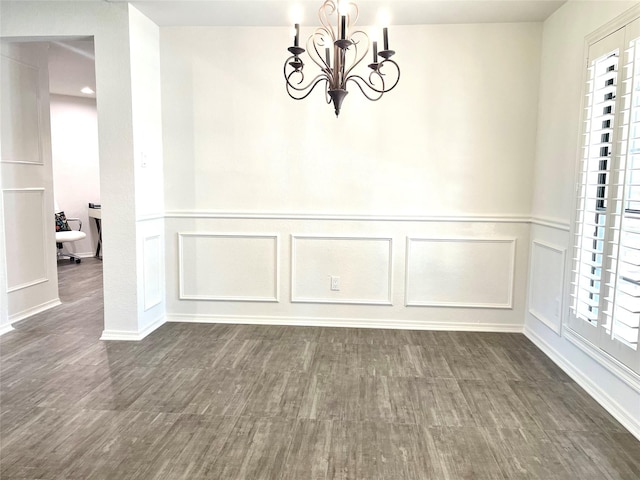 unfurnished dining area with a decorative wall, a chandelier, plenty of natural light, and dark wood-type flooring