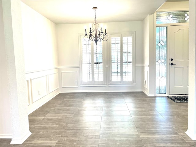 unfurnished dining area featuring a wainscoted wall, a decorative wall, wood finished floors, and a notable chandelier