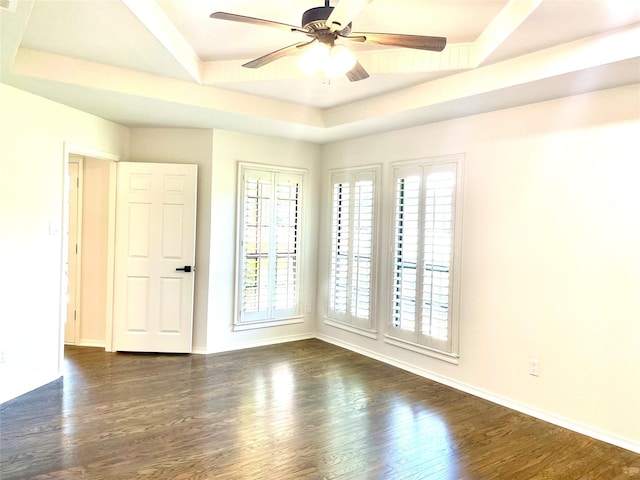empty room with a raised ceiling, ceiling fan, baseboards, and dark wood finished floors