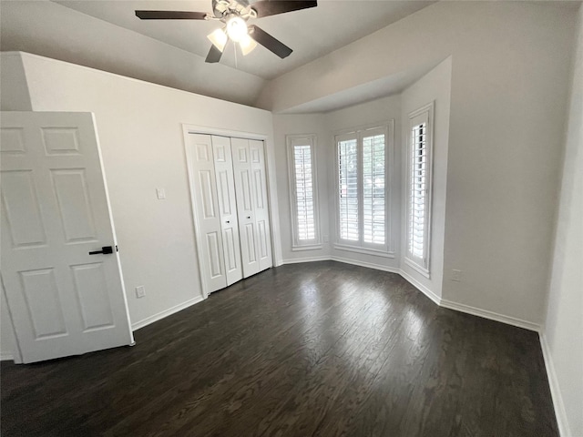 unfurnished bedroom featuring a ceiling fan, dark wood finished floors, baseboards, a closet, and lofted ceiling