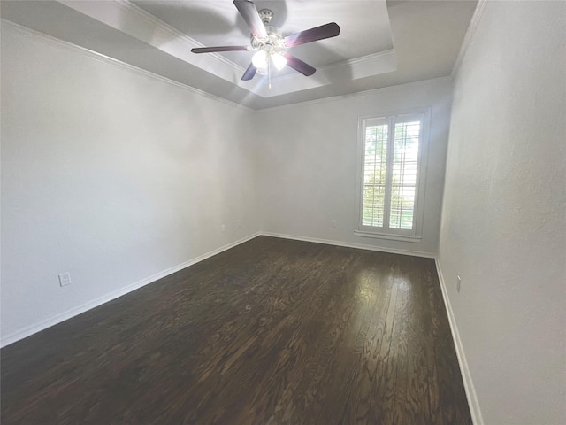 unfurnished room with a ceiling fan, dark wood-style flooring, crown molding, a raised ceiling, and baseboards