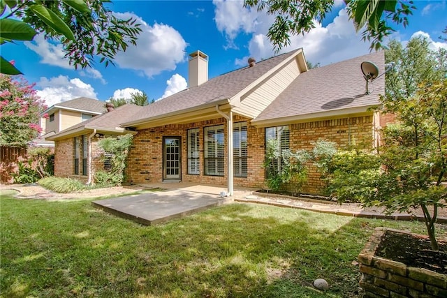 rear view of house featuring a patio, roof with shingles, a chimney, brick siding, and a yard