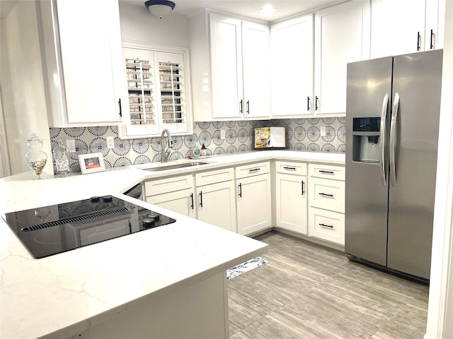 kitchen with stainless steel refrigerator with ice dispenser, black electric stovetop, a sink, and white cabinetry