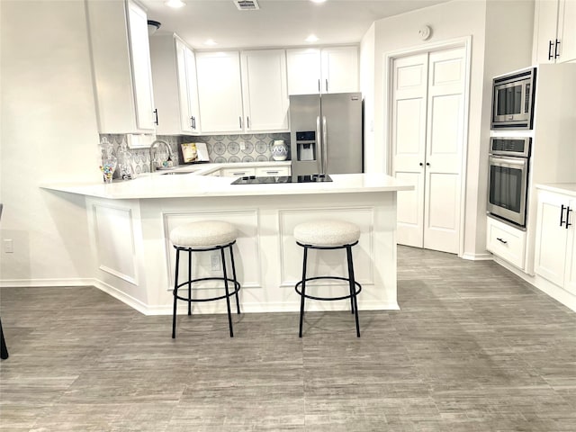 kitchen featuring decorative backsplash, a sink, light countertops, a peninsula, and stainless steel appliances