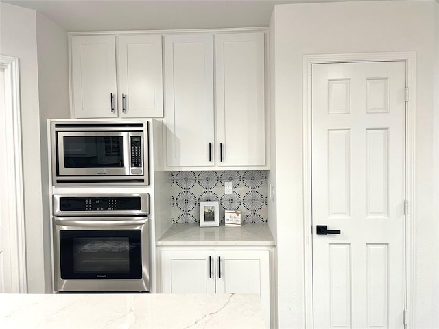 kitchen featuring light stone counters, decorative backsplash, appliances with stainless steel finishes, and white cabinets