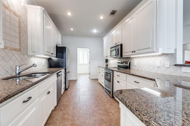 kitchen featuring white cabinets, appliances with stainless steel finishes, a sink, dark stone countertops, and visible vents