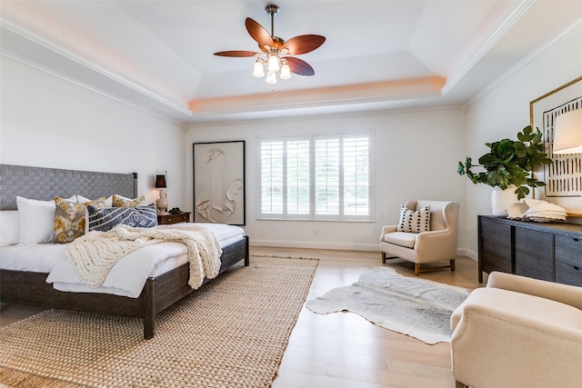 bedroom with crown molding, a ceiling fan, a tray ceiling, and light wood-type flooring