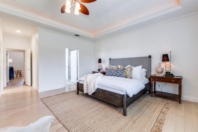 bedroom featuring a raised ceiling, light wood-style flooring, baseboards, visible vents, and ornamental molding