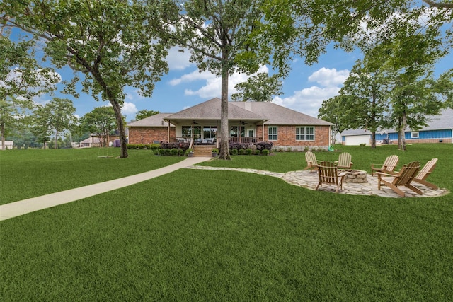 rear view of property featuring a lawn, ceiling fan, an outdoor fire pit, and brick siding