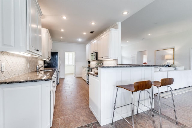 kitchen with a breakfast bar area, appliances with stainless steel finishes, tasteful backsplash, white cabinets, and ornamental molding