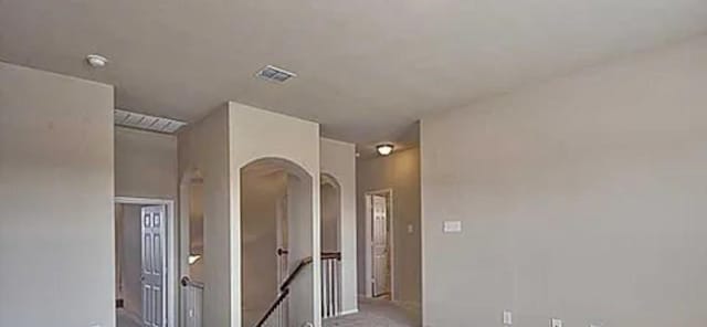 hall featuring arched walkways, visible vents, and an upstairs landing