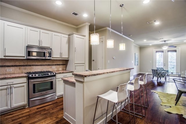 kitchen with crown molding, appliances with stainless steel finishes, a kitchen island, and visible vents