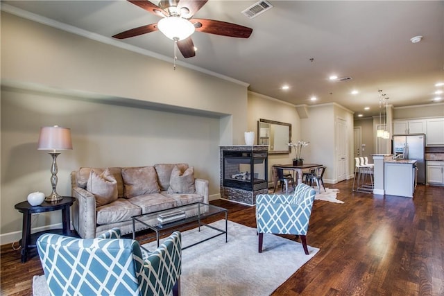 living room featuring a ceiling fan, visible vents, baseboards, ornamental molding, and dark wood-type flooring