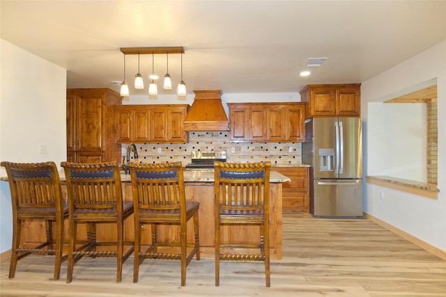 1112 Hillside Dr, Gainesville, TX 76240 - kitchen featuring a kitchen breakfast bar, light wood-type flooring, brown cabinets, premium range hood, and stainless steel appliances