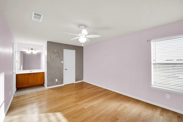 unfurnished bedroom with visible vents, ensuite bathroom, baseboards, ceiling fan, and light wood-style flooring