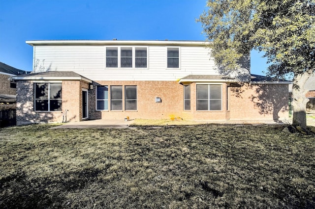 rear view of property with brick siding, a lawn, and a patio